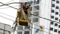 Seorang pekerja memperbaiki lampu penerangan jalan.