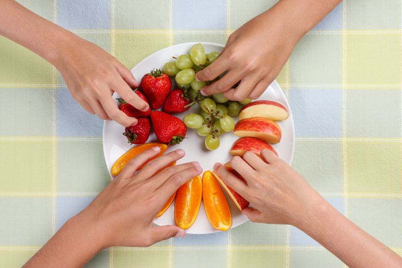 Plate full of fruit being snatched up by four children.