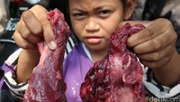 Seorang anak menunjukan daging kurban yang ia dapat.
