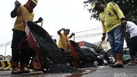 Petugas menumpahkan aspal untuk menutup jalan yang berlubang.