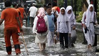 Para pelajar melintas di jalan yang terendam banjir. Beberapa di antara mereka tampak melepas sepatunya.