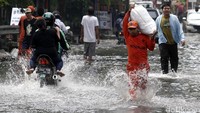 Pengendara dan pejalan kaki melintas di jalan yang terendam banjir.