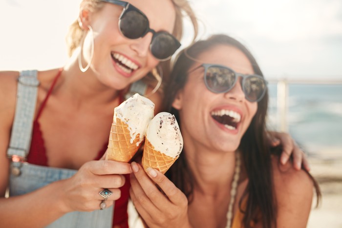 Two young female friends having fun and eating ice cream. Cheerful young women eating icecream outdoors.
