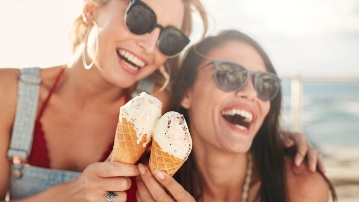 Two young female friends having fun and eating ice cream. Cheerful young women eating icecream outdoors.