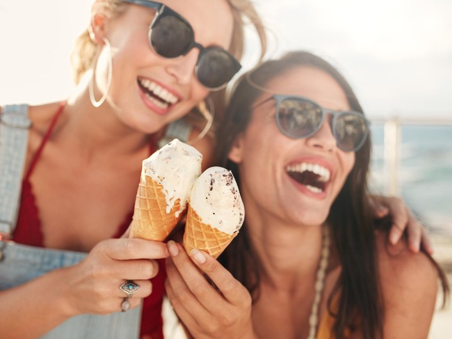 Two young female friends having fun and eating ice cream. Cheerful young women eating icecream outdoors.