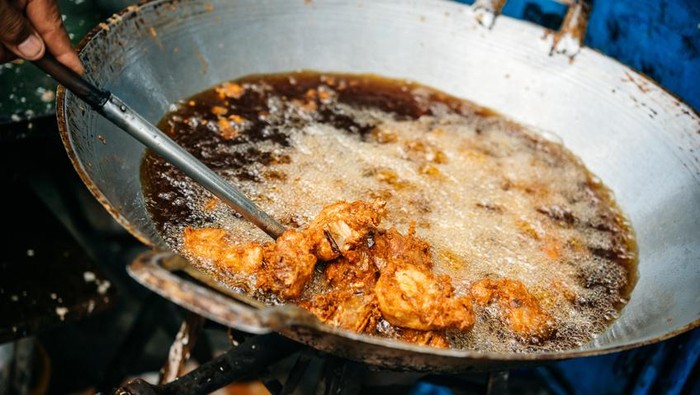 A vendor cooks deep fried chicken in the street in Bangkok, Thailand.
