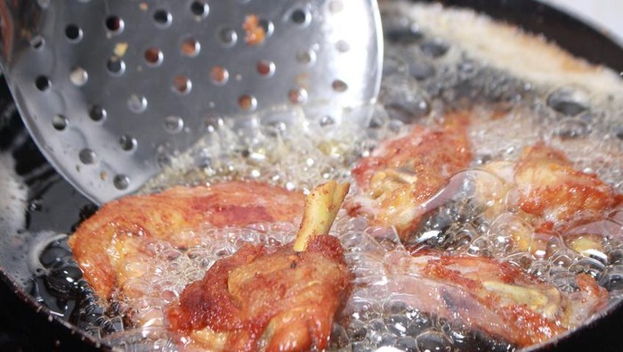 A vendor cooks deep fried chicken in the street in Bangkok, Thailand.