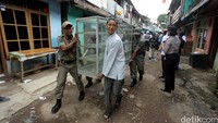 Seorang warga dan Salpol PP terlihat menggotong lemari kaca.