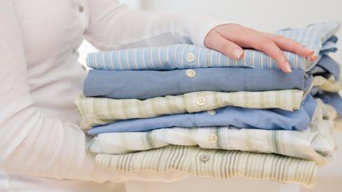 Woman carrying stack of folded shirts, close-up, mid section