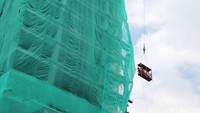Petugas memberi selubung jala transparan warna hijau di gedung yang akan dirobohkan.