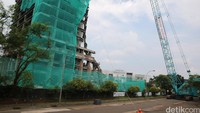 Petugas dan alat berat membungkus gedung mangkrak dengan jala transparan sebelum dirobohkan.