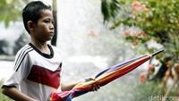 Seorang anak mengais rezeki di tengah hujan dengan menawarkan jasa ojek payung.