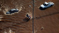 Empat orang warga melintas di jalan yang terendam banjir setinggi lutut. Chris Keane/Reuters/detikFoto.