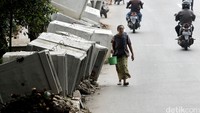 Pejalan kaki melintas di depan proyek perbaikan saluran air.