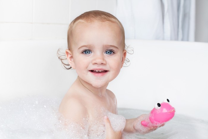 185587667 Baby Bath portrait of an cute little baby girl having fun in bath tube, looking at camera