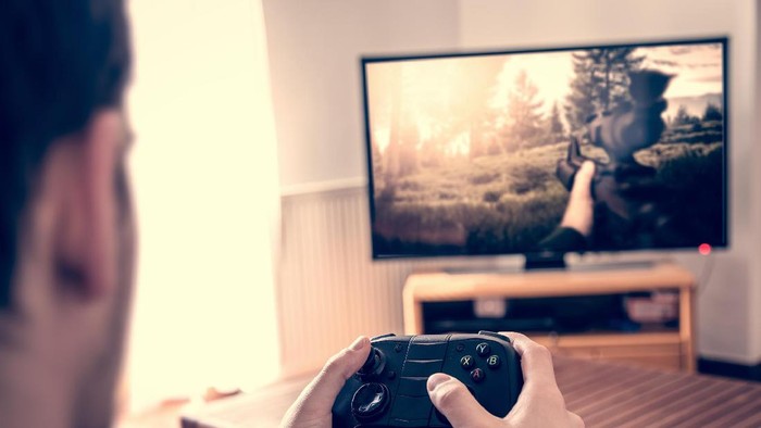 Hands holding game pad and playing shooter game on tv screen.