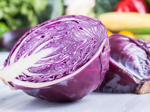 Close up photo of edible vegetables - a red cabbage with some vegetables in the background on a solid light blue wooden table