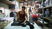 Seorang pegawai jasa laundry menyetrika baju pelanggan.