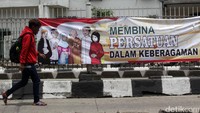Seseorang melintas didepan spanduk himbauan untuk menjaga persatuan umat beragama di Stasiun Jatinegara, Jakarta Timur.