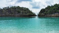 Ketika boat berbelok di sebuah celah dua karang yang menjulang, arus air mendadak lebih tenang. Ternyata boat sudah masuk ke sebuah laguna cantik yang dipagari karang yang membukit di sekelilingnya (Sukma/detikTravel)