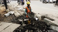 Seorang pekerja membersihkan sisa aspal untuk dijadikan lahan trotoar.