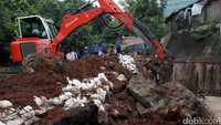 Sebuah kendaraan backhoe juga terlihat sedang menguruk tanah di lokasi longsoran.