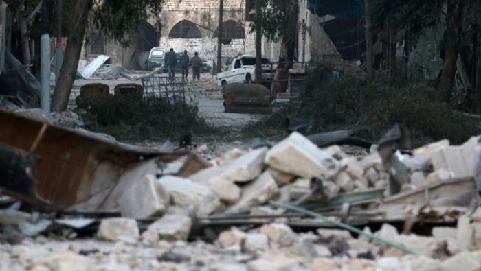 Orang-orang berjalan di dekat puing-puing bangunan yang rusak, di daerah terkepung dikuasai pemberontak Aleppo, Suriah