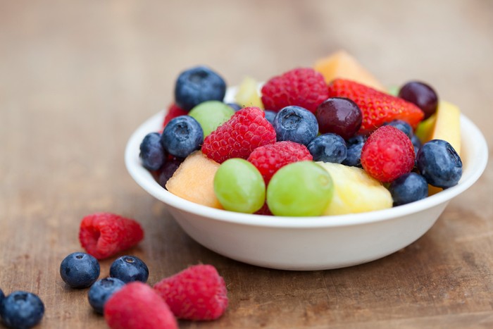Fruit salad in white bowl. Blueberries, rasberries, melon, grapes and strawberries.