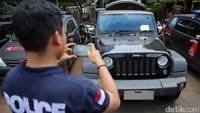 Seorang anggota polisi sedang memotret barang bukti berupa mobil Jeep Rubicon.
