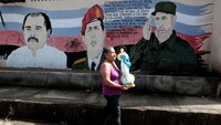 Seorang wanita nampak melintas di depan mural Fidel Castro, mantan Presiden Venezuela Hugo Chavez, dan Presiden Nikaragua Daniel Ortega di Nicaragua (27/11/2016). REUTERS/Oswaldo Rivas.