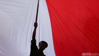 Seorang peserta aksi berada di naungan merah putih raksasa.