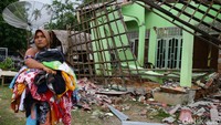 Seorang warga melintas di depan rumah yang ambruk akibat gempa.