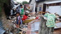 Tiga orang anak berdiri di atas puing-puing bangunan.