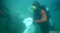 Seorang penyelam membawa karung putih berisi sampah.
