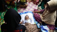 Seorang bayi ditidurkan di tenda pengungsian. Bayi tersebut tampak ditunggui oleh ibunya dan tim trauma healing.