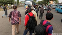 Calon penumpang menunggu bus di pinggir jalan.