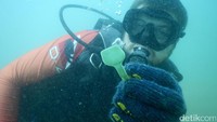 Seorang penyelam menunjukkan sampah yang diambil dari dasar laut.