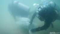 Dua orang penyelam membawa karung berisi sampah ke pelabuhan.