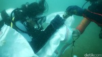 Para penyelam mengumpulkan sampah di dalam karung putih.