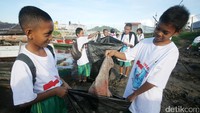 Para siswa memasukkan sampah ke kantong plastik besar.