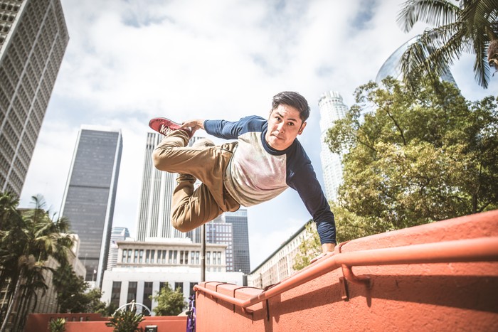 Two young male parkour freerunners jumping over a wall.