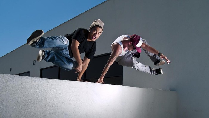 Two young male parkour freerunners jumping over a wall.