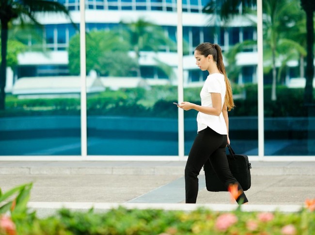 469337244 Cropped view of business woman walking in city street with laptop bag, chatting on mobile phone and going to work in the morning