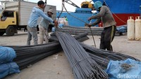 Beberapa pekerja menurunkan besi beton dari atas kapal.