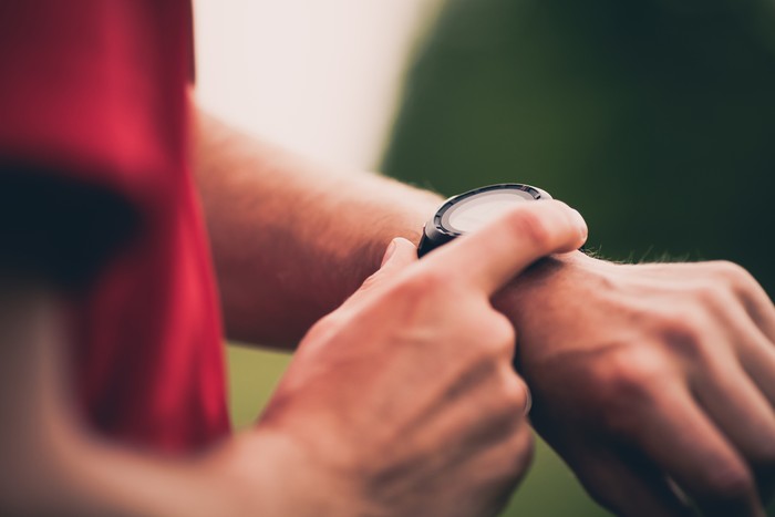 Runner using heart rate monitor training running, smartwatch checking performance or GPS. Man athlete looking at stopwatch. Healthy runner closeup on trail running workout. Wearable technology for tracking activity.