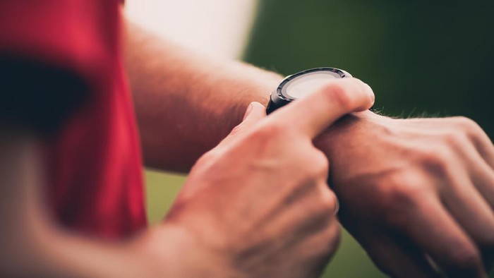 Runner using heart rate monitor training running, smartwatch checking performance or GPS. Man athlete looking at stopwatch. Healthy runner closeup on trail running workout. Wearable technology for tracking activity.