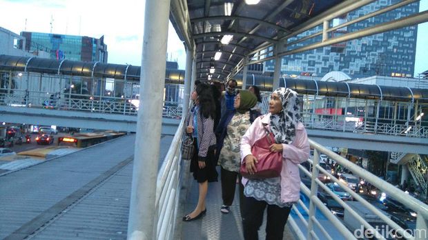 Pengguna bus TransJakarta melihat aksi pria memanjat baliho di Harmoni, Jakarta Pusat, Selasa (20/12/2016)