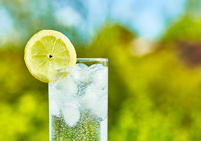 Air soda dan irisan lemon dalam gelas dengan es, hari yang cerah - fokus sempit di tengah gelas