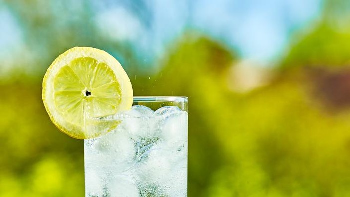 Sparkling water and lemon slice on glass with an ice, sunny day - narrow focus on middle of the glass