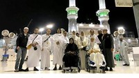 Jupe dan Ria tampak duduk di kursi roda saat berpose di depan Masjidil Haram bersama keluarga dan rekannya. (Dok. Instagram/juliaperrezz)